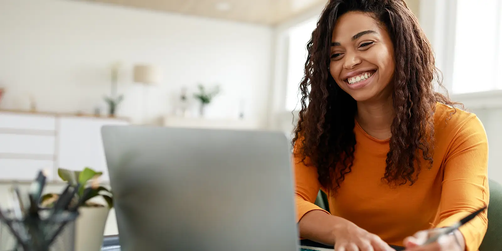 woman sitting at desk using laptop and writing in notebook