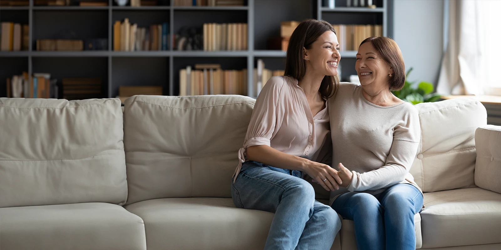A mother and daughter sitting on a couch laughing together.
