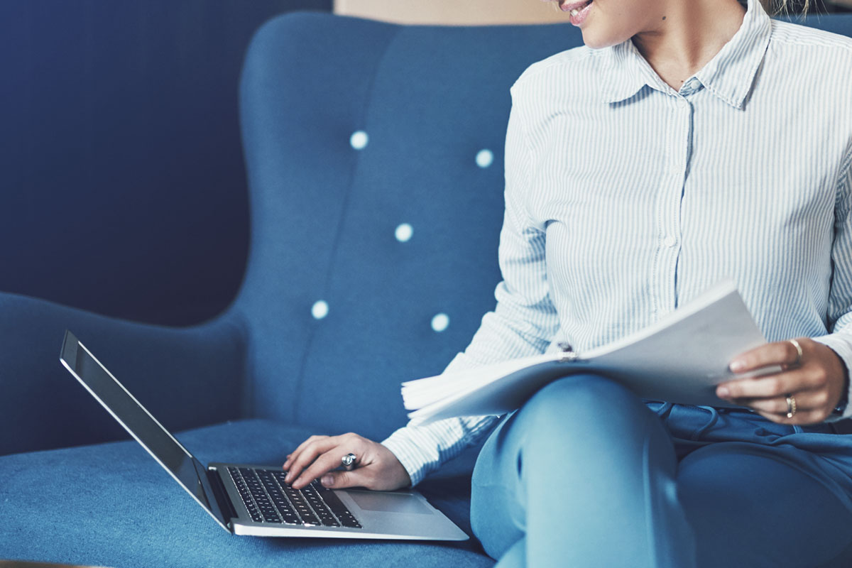 Person sitting on a blue couch working on a laptop