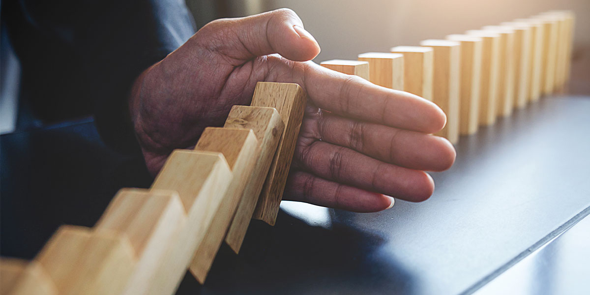 Close up of a persons hand stopping wooden dominos from falling