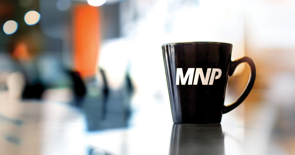 A black mug with the MNP logo on it with a blurred background