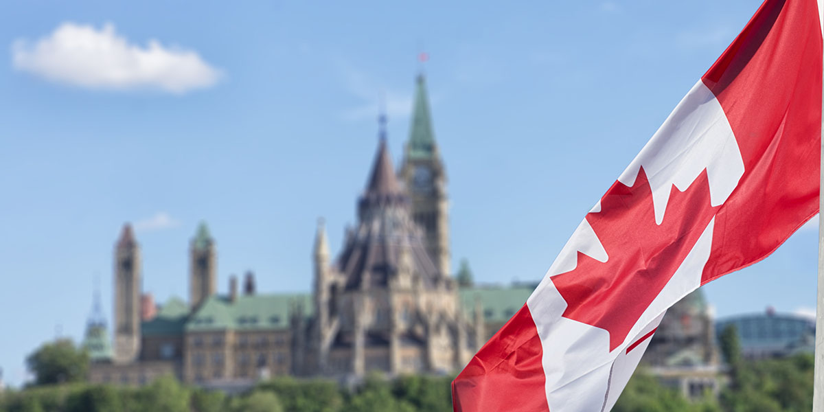 Canadian flag waving in the wind with a government building in the background