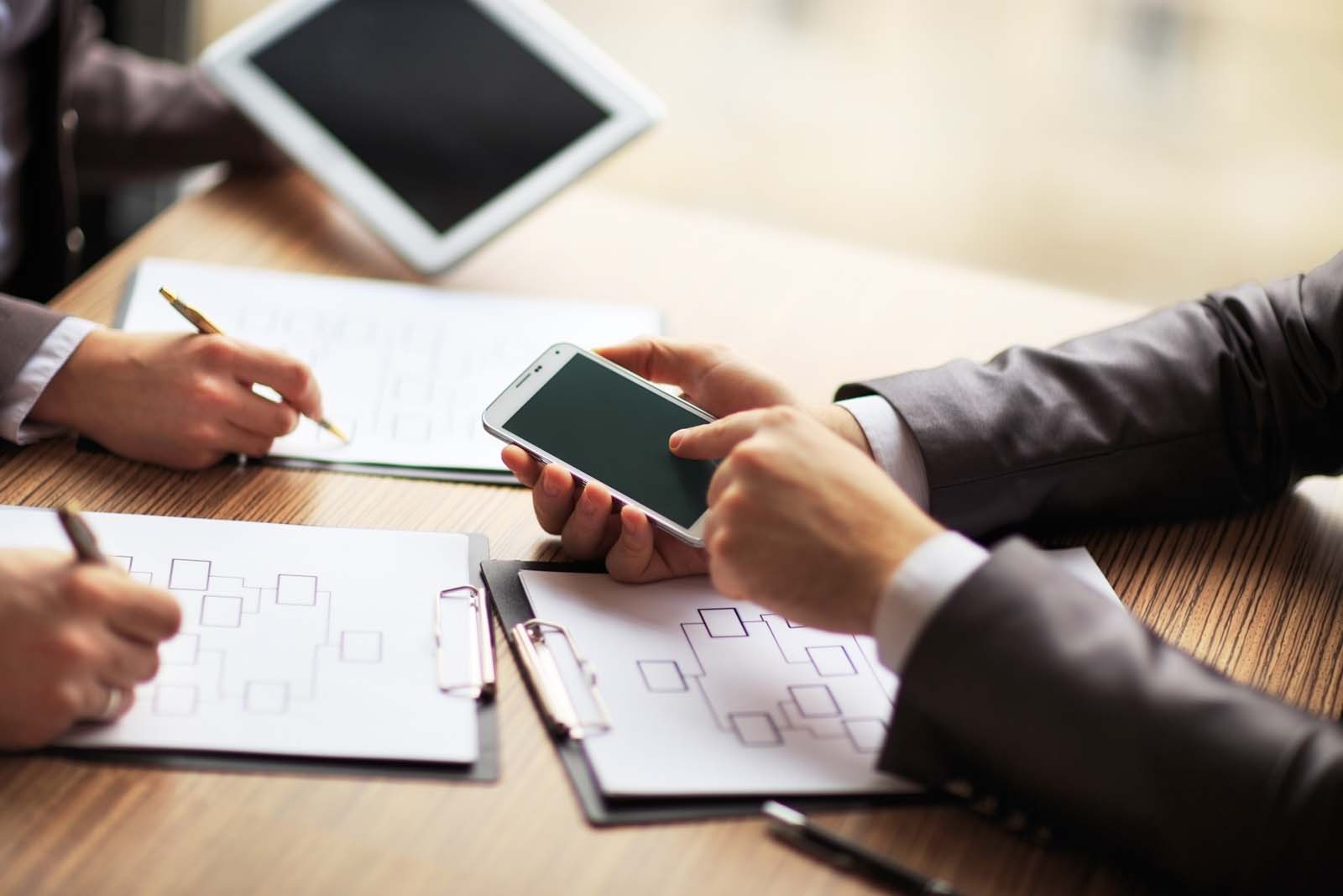 people in a board room working on phones with papers on the table