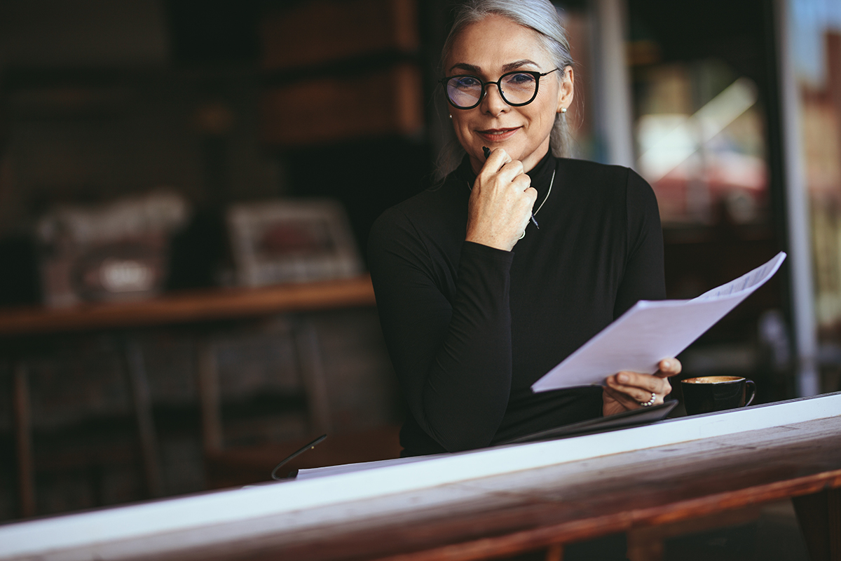 Woman sitting at a table smiling and holding a piece of paper