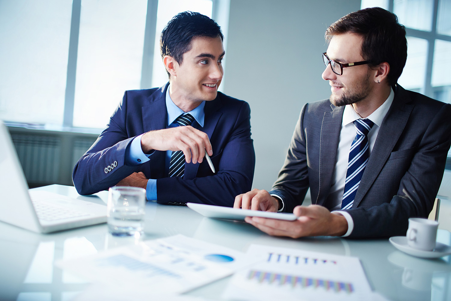 Two businessmen working together using a laptop and tablet.