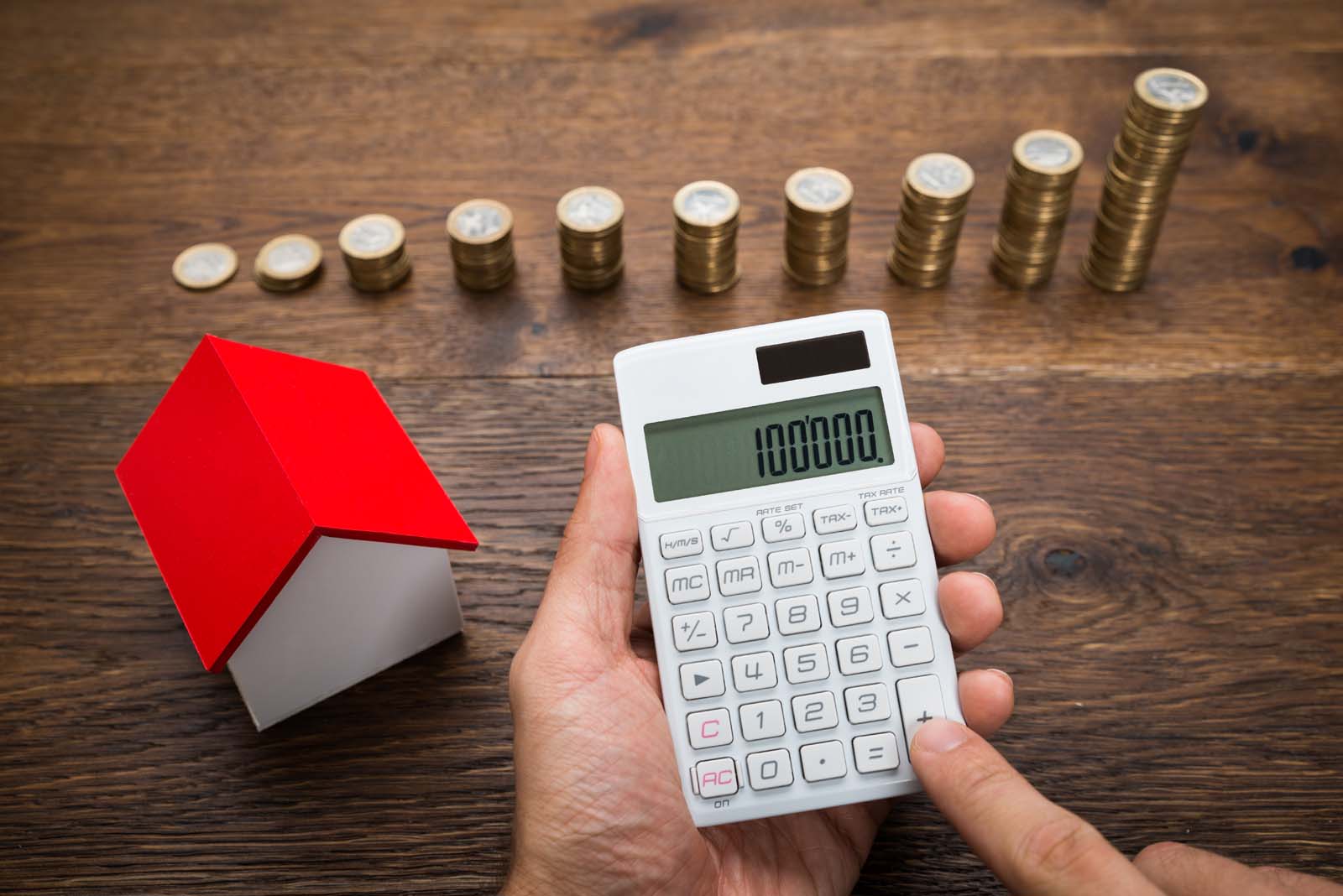 someone working on a calculator by a small house and stacks of coins