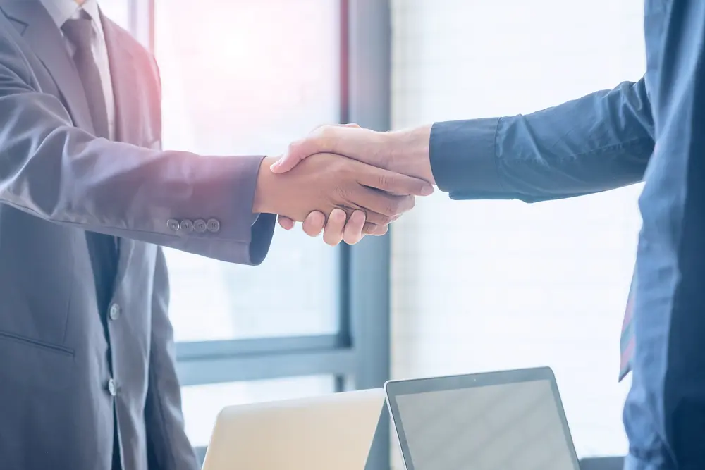 Two businessmen shaking hands over laptops