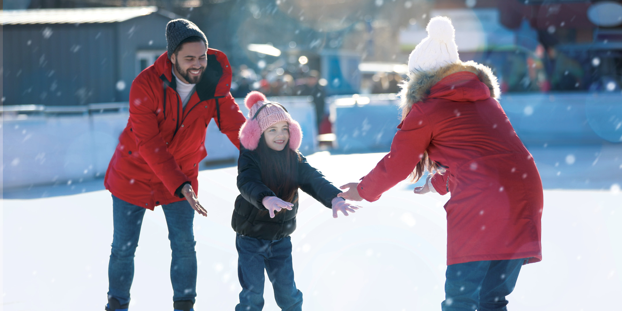 A family of three skating on an outdoor skating rink together.