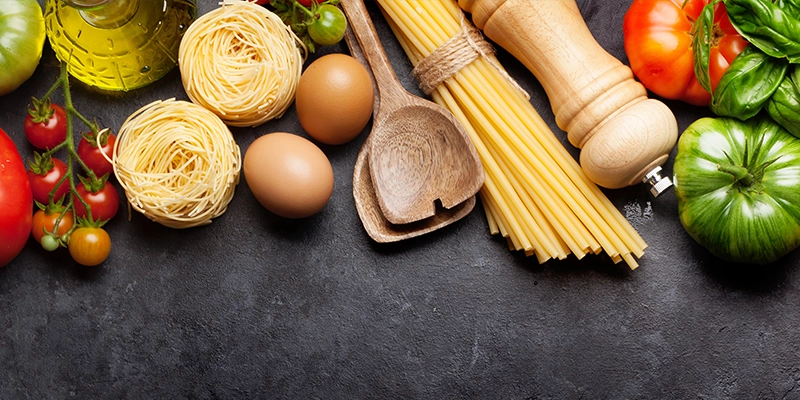 A collection of dried pasta and vegetables together on a kitchen table.