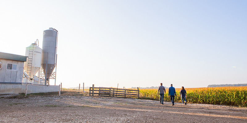 A family walking along a farm field with a white barn in the background.