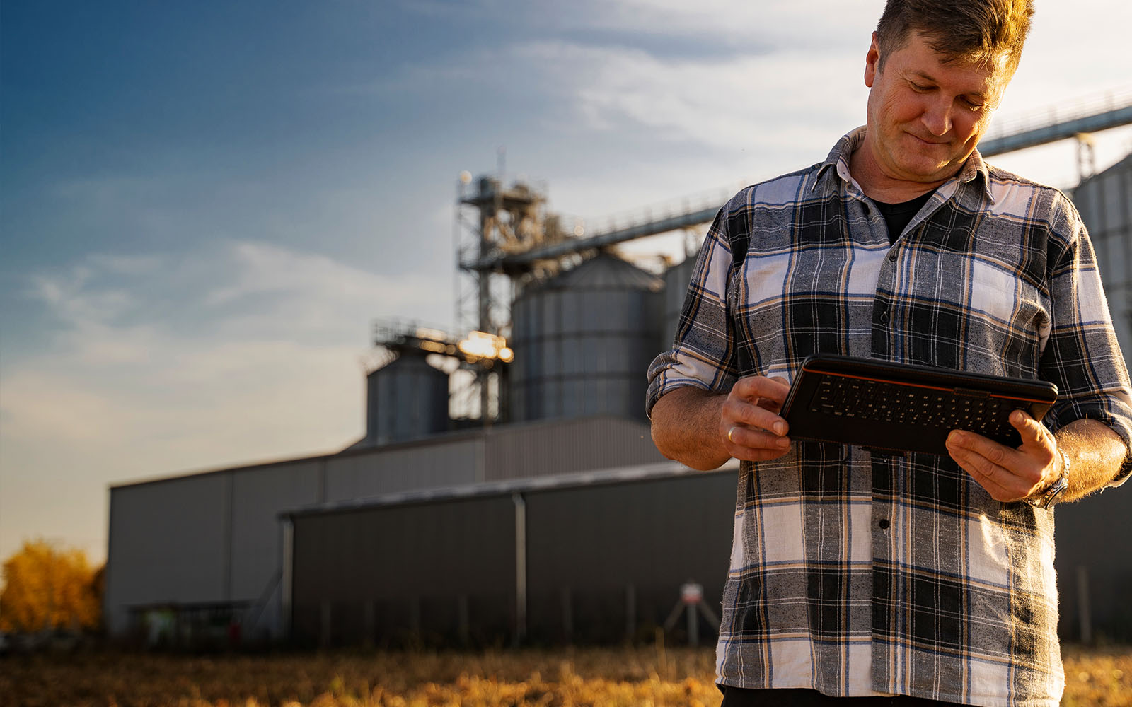 farmer working on a tablet with a grain silo in the background