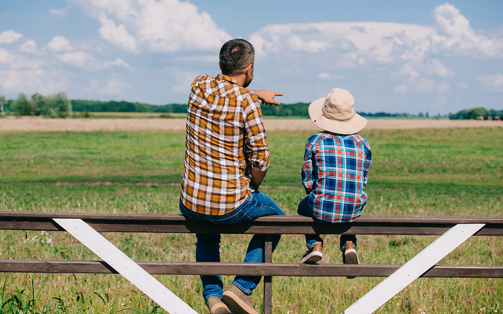 Father and son sitting on a fence post overlooking their family farm