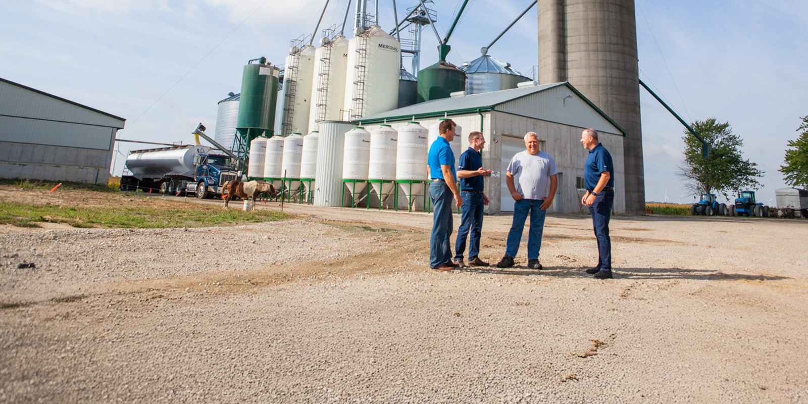 Group consulting on farm with equipment and building in the background
