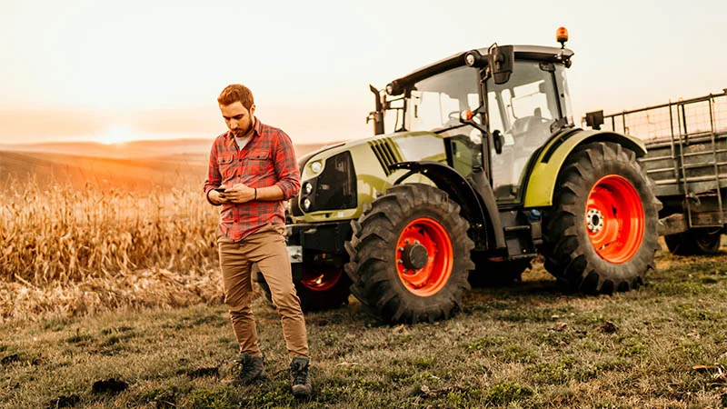 Homme utilisant un téléphone portable devant un tracteur dans un champ de blé