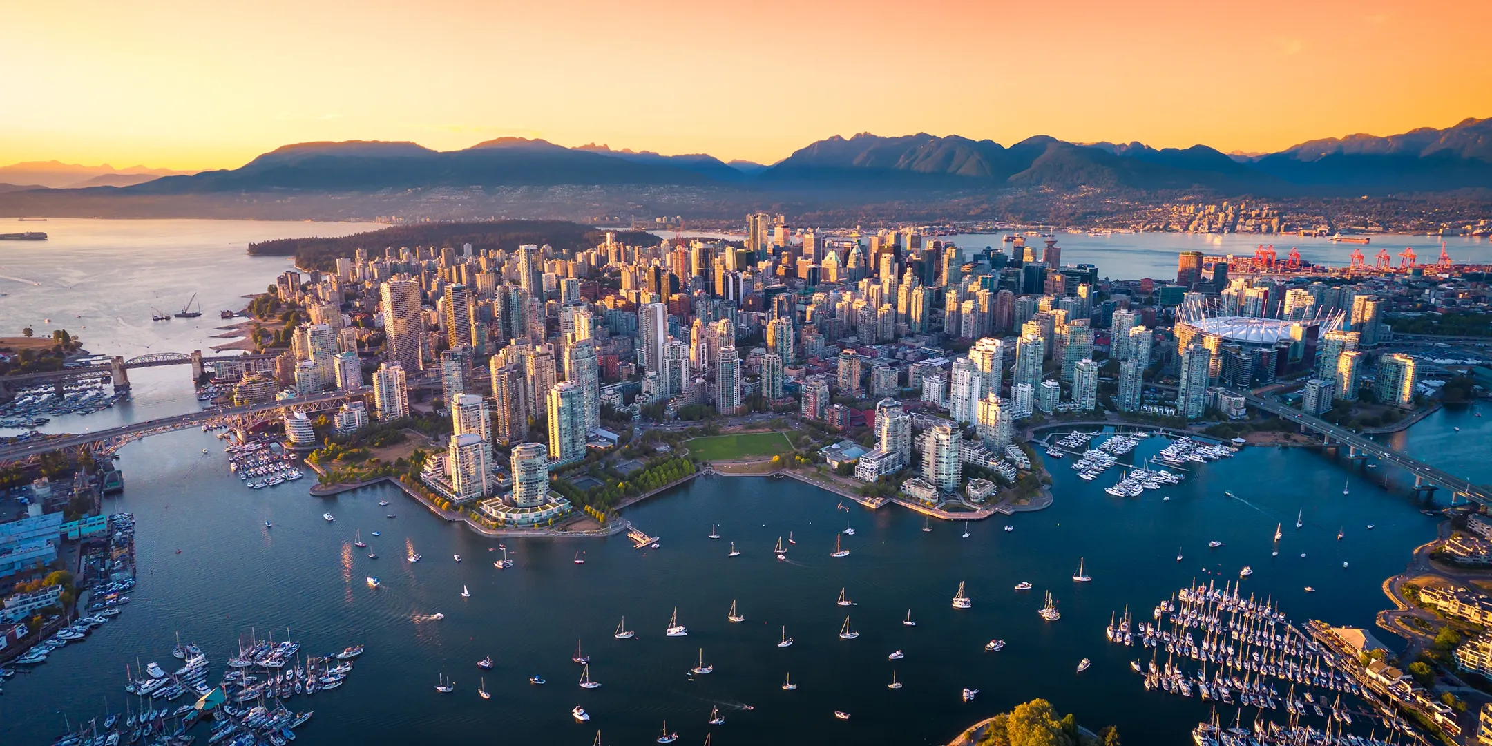 A sky photo of Vancouver city showing boats, buildings and mountains off in the distance