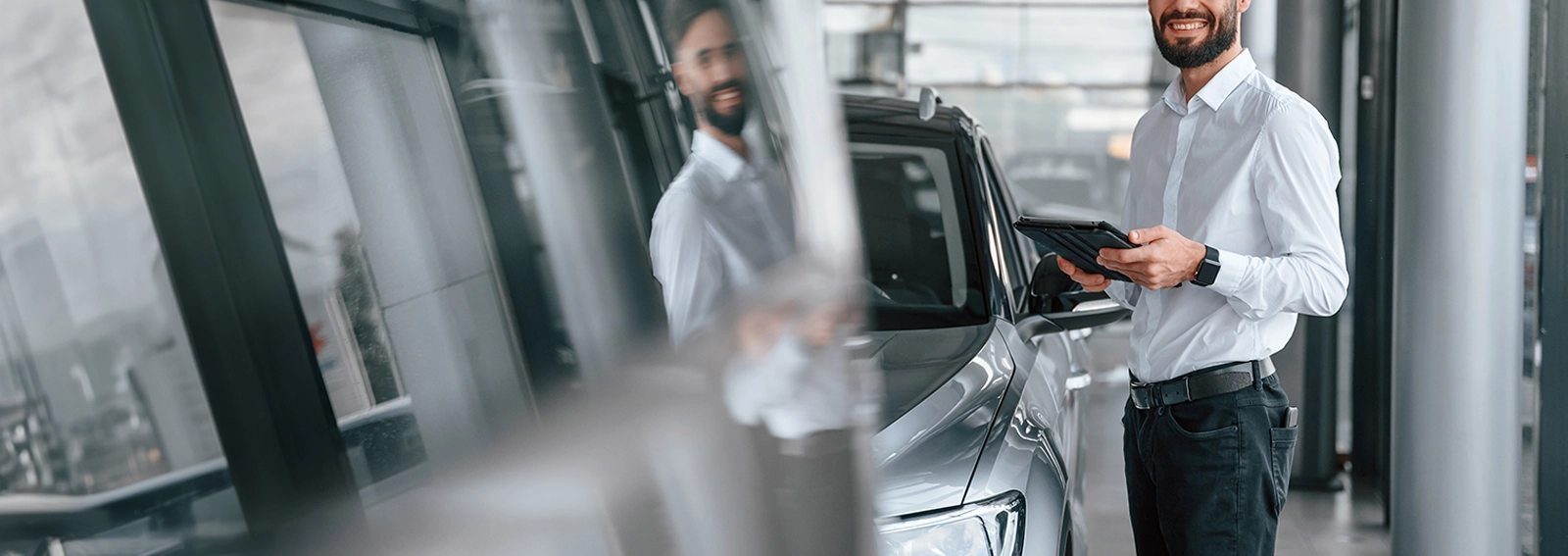 smiling dealership employee standing by a white car