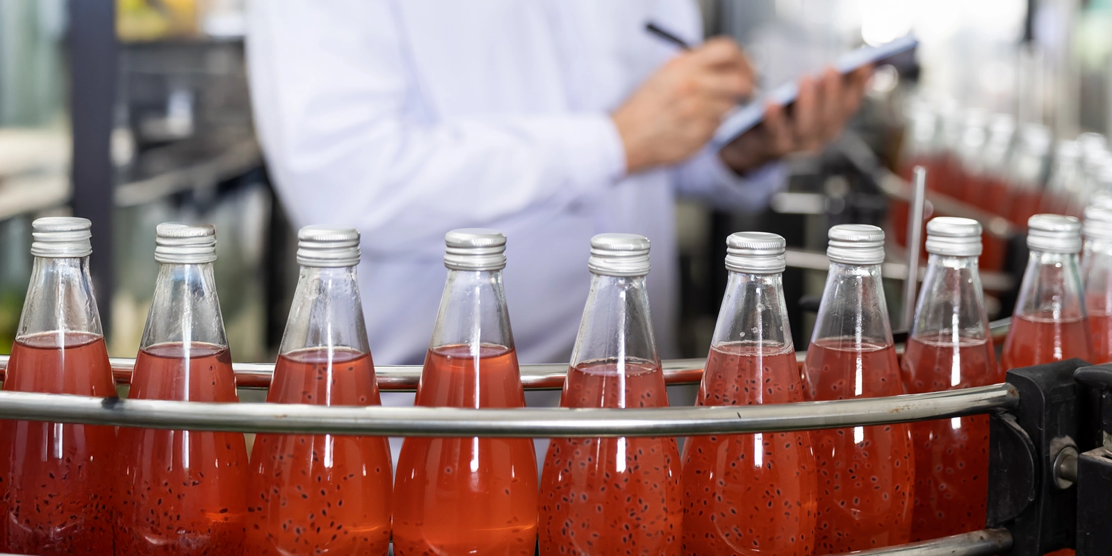 Hands of worker writing notes about product of drink on the conveyor belt in the beverage factory