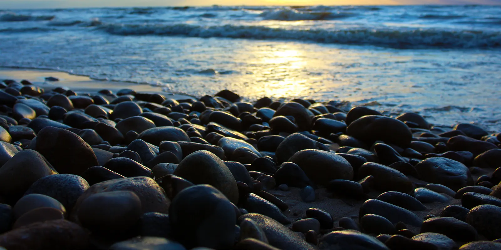 A serene beach at sunset, adorned with rocks and gentle waves lapping against the shore.