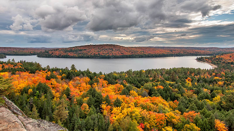 A wide view of a big lake surrounded by green, orange and yellow trees