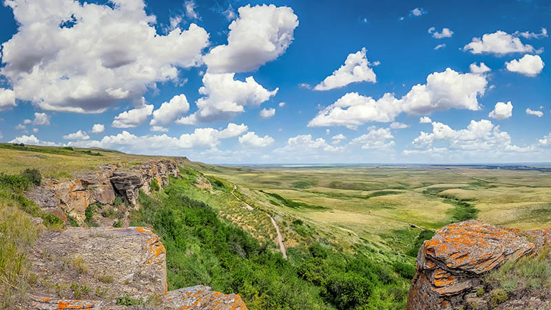 View of cliffs and green prairies under a cloudy blue sky  