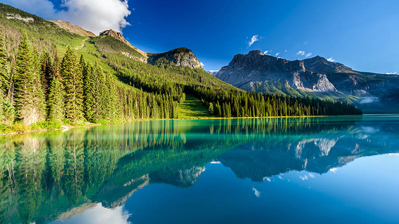 A mountain range and green forests with a reflective lake in the foreground