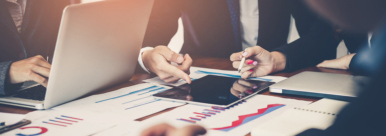 Group of business workers pointing to a tablet and graphs on a table.