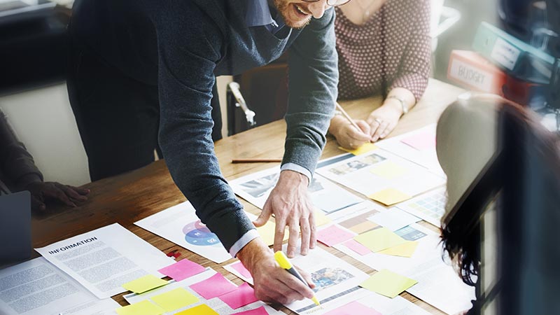 Trois personnes collaborent autour d'une table recouverte de paperasse