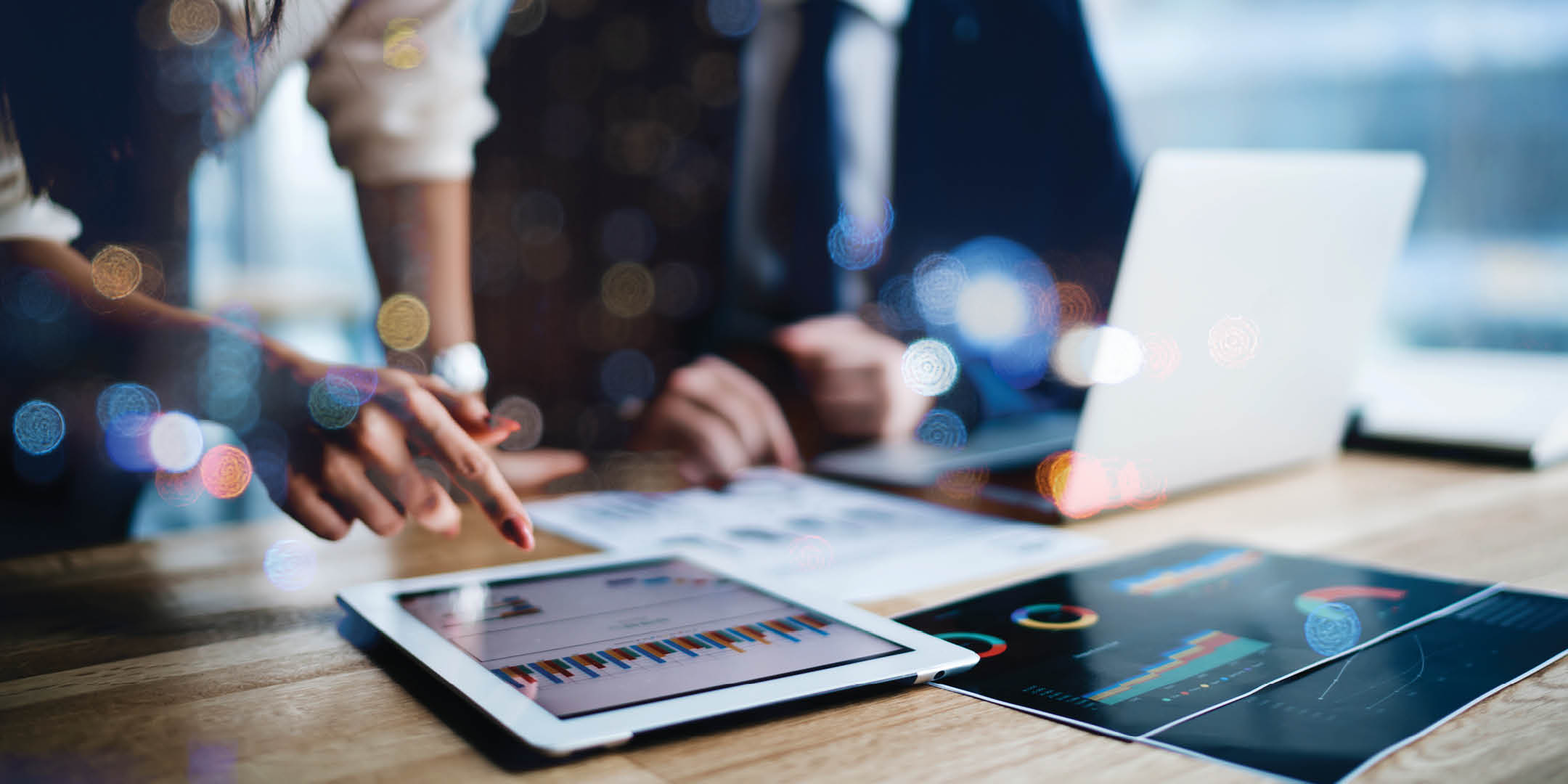 Man and woman sitting at a desk reviewing documents and looking at data on an ipad