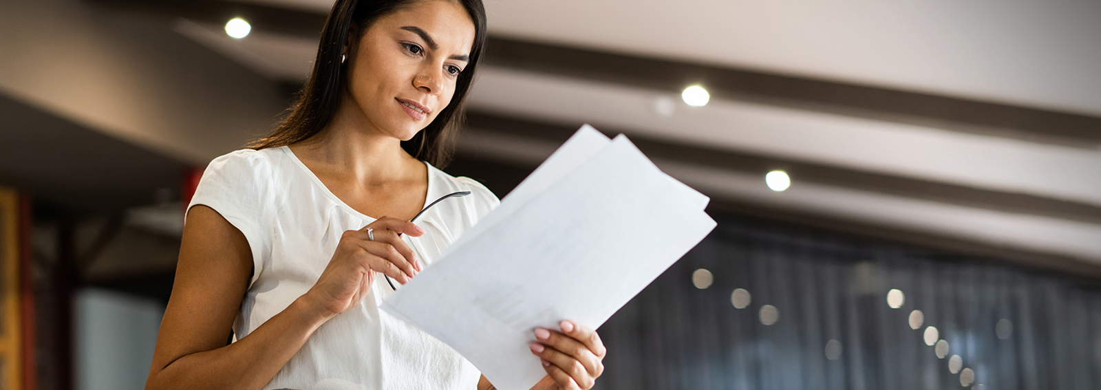 Woman examining documents while standing near table in office.