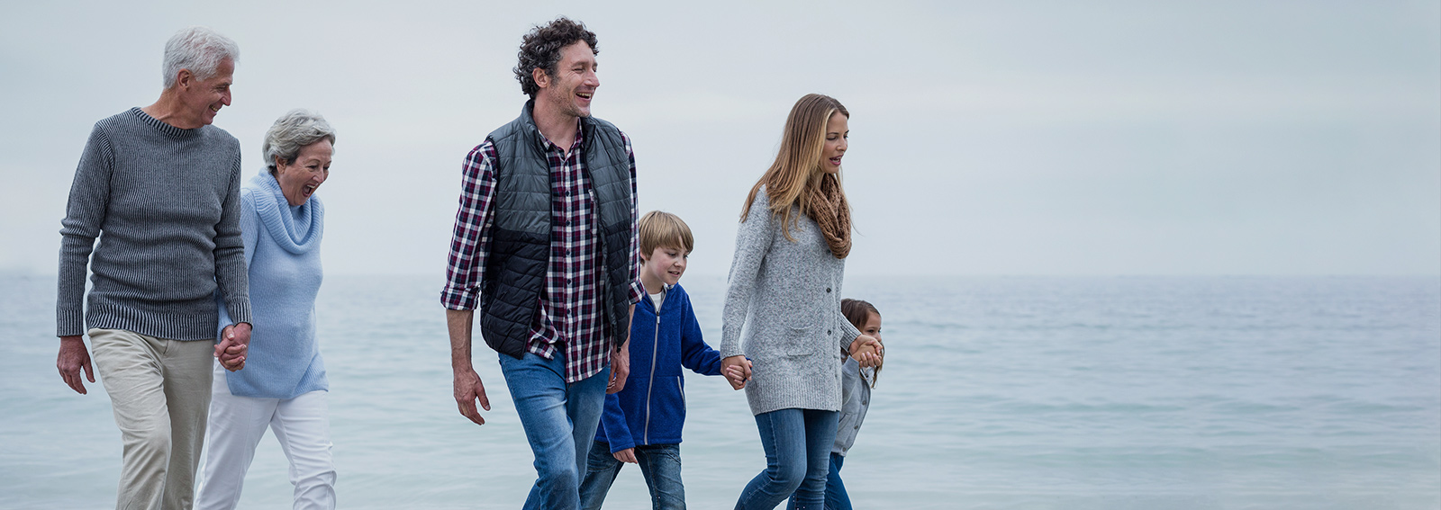 Three Generation Family Walking Along Sandy Beach.