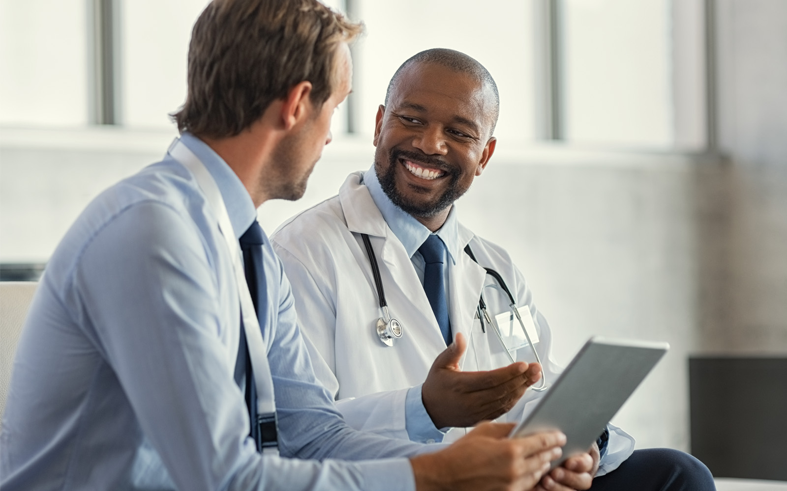 Two mature smiling doctors having discussion about patient diagnosis holding digital tablet