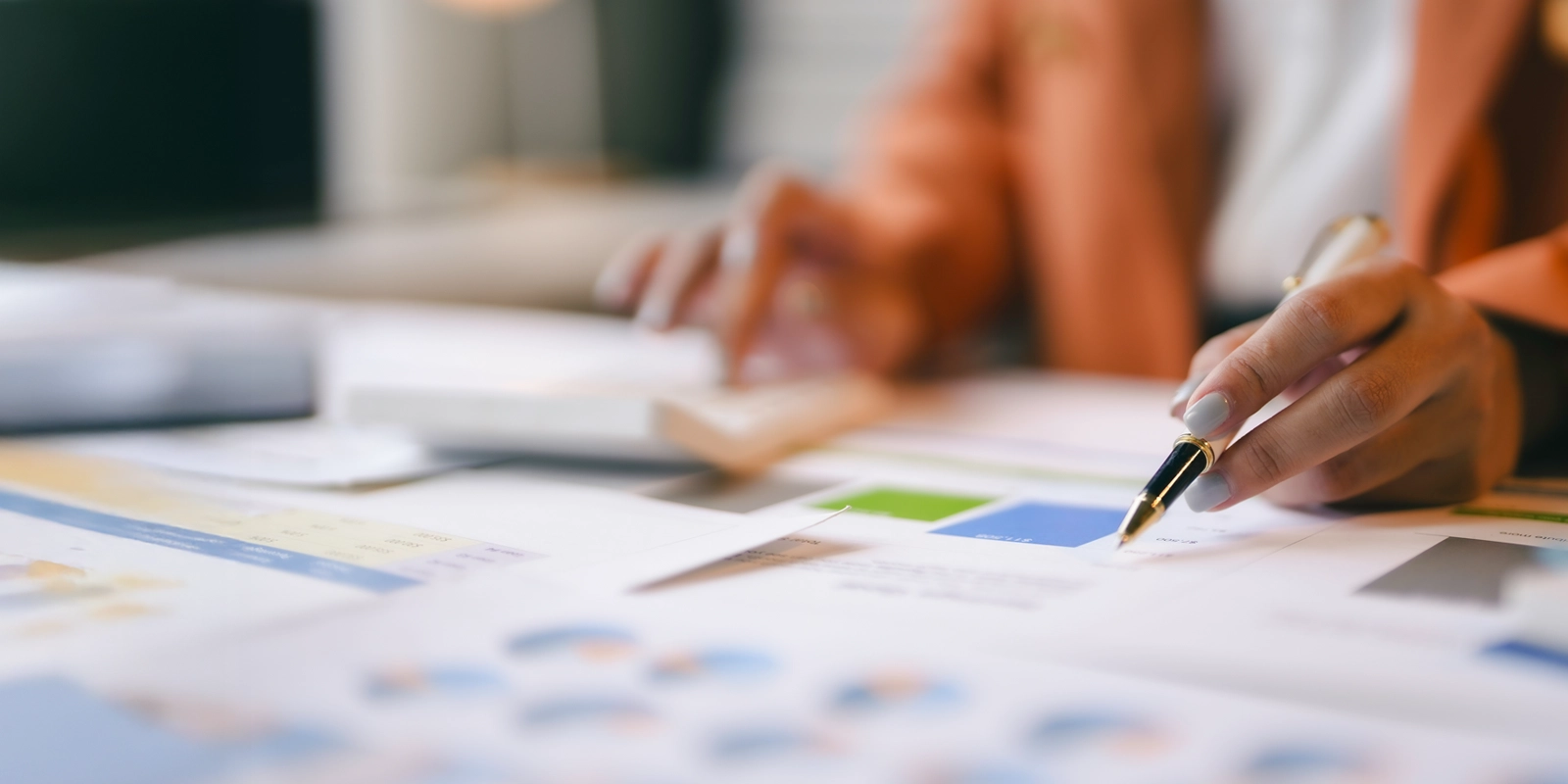 Businesswoman analyzing financial charts at desk using calculator and pen