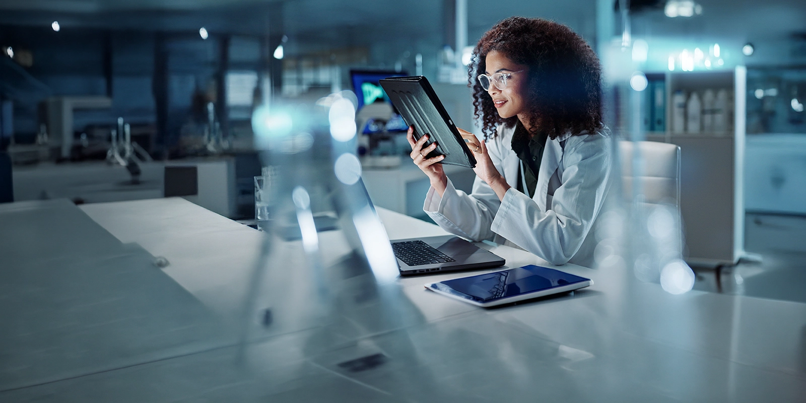 Person in lab coat using tablet beside laptop in modern workspace