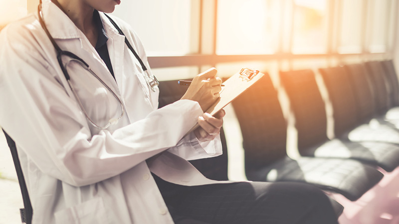 Close up of a doctor sitting in a chair holding a clipboard 