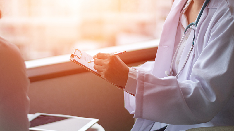 Gros plan d'un médecin écrivant sur un presse-papiers