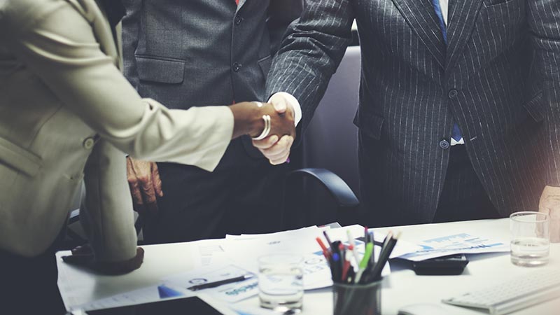 Close up of two people shaking hands over a desk covered in paperwork