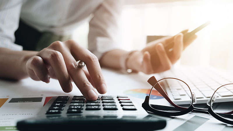 Close up of a person using a calculator and a pair of glasses