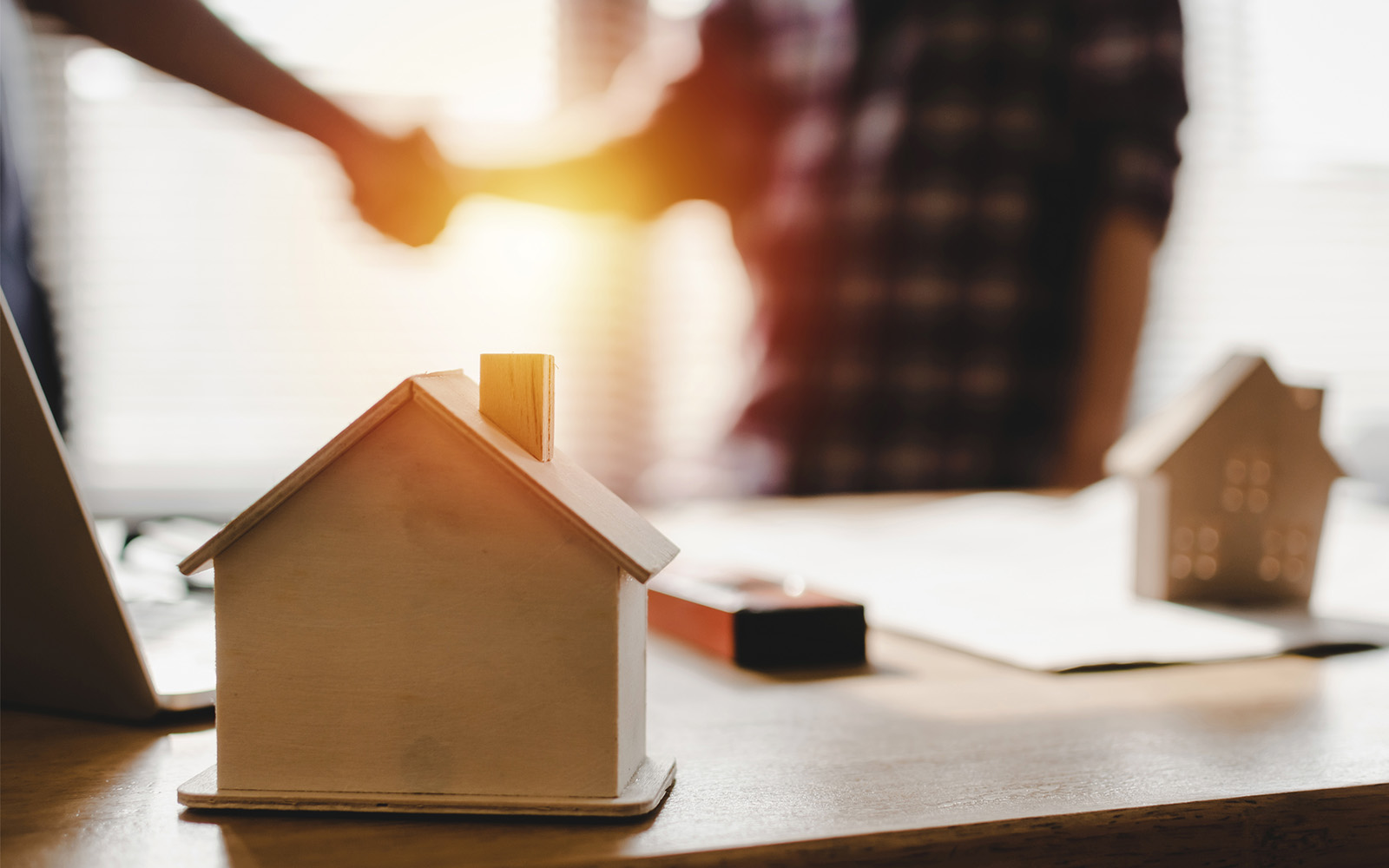 une maison en bois sur une table avec des gens se serrant la main en arrière-plan