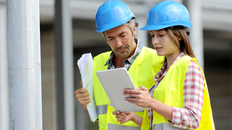 Two construction workers in blue hard hats and yellow safety vests