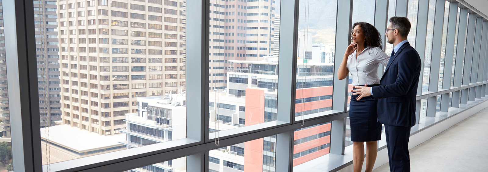 Two professionals looking out a window in a downtown city.