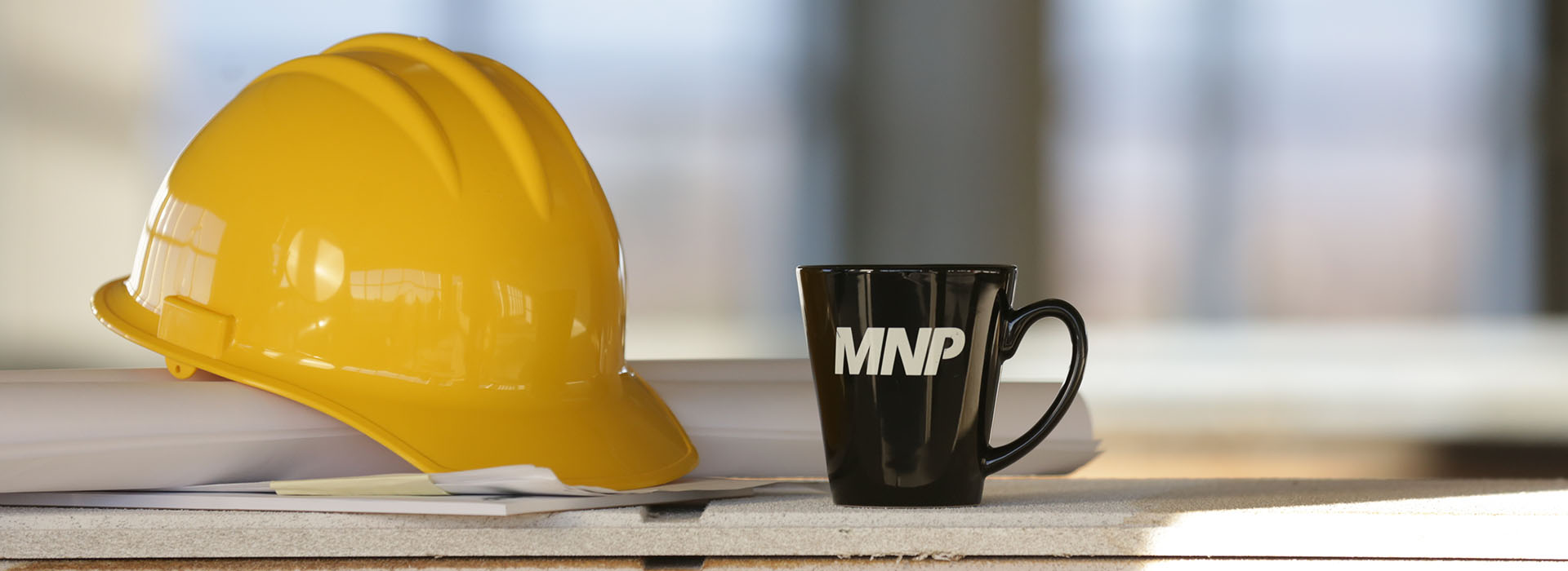 Yellow hard hat sitting on a stack of drafting papers next to MNP mug