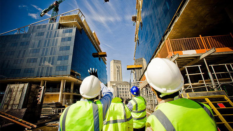 Ground view of a construction site with four workers in hard hats and safety vests