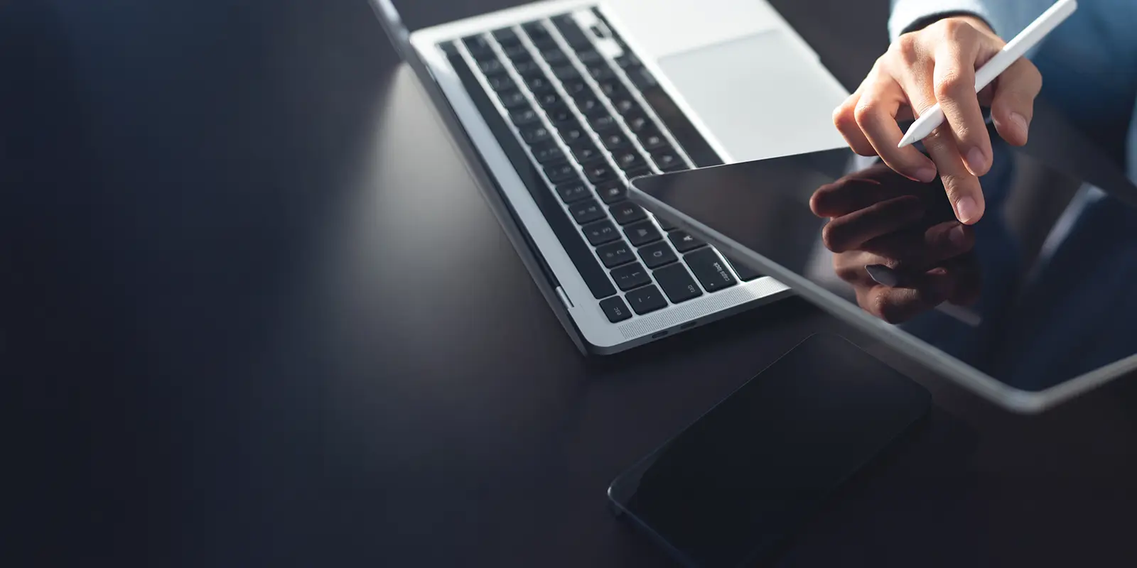 Person on a tablet along with a cell phone and a computer