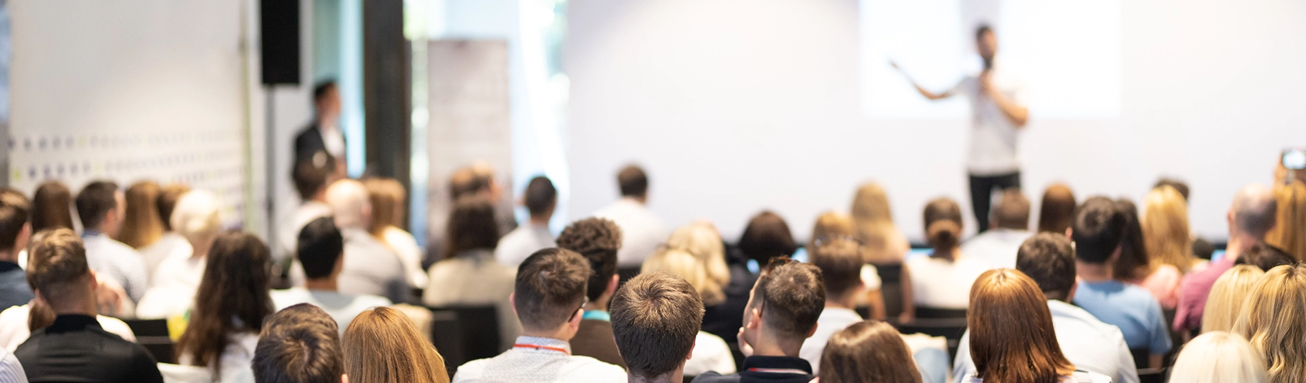 Un grand groupe de personnes assises dans une salle de conférence, faisant face à un orateur qui se tient debout et présente à l'avant de la salle.