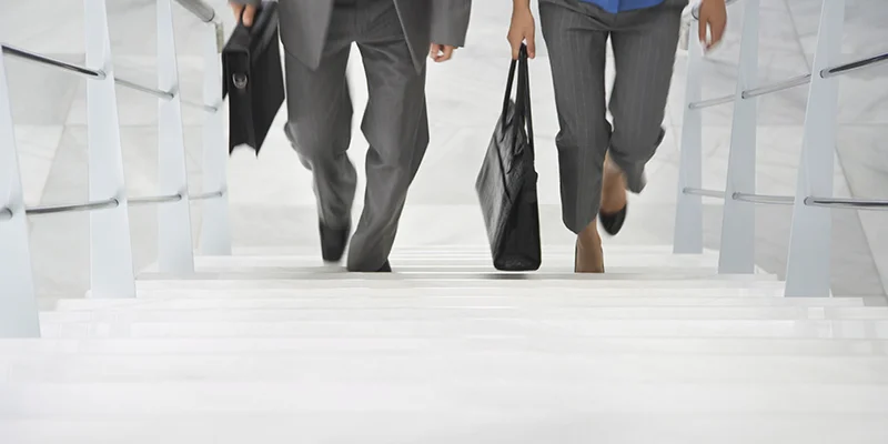 Man and woman professionals walking up stairs together.