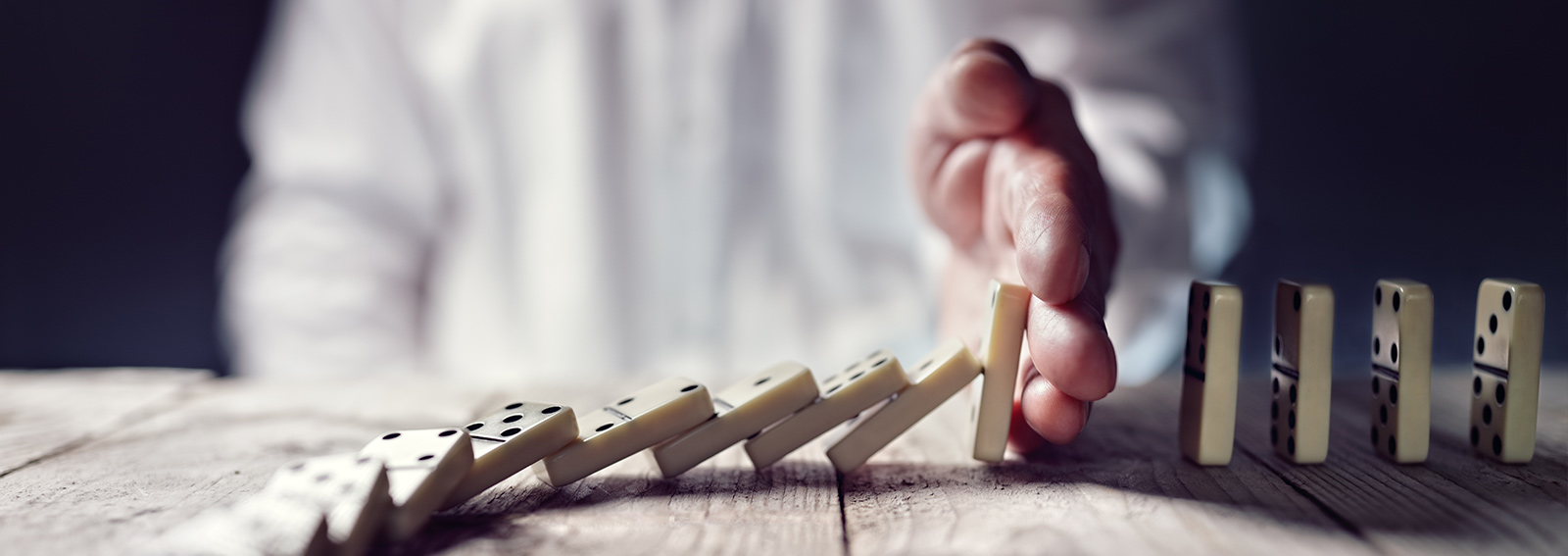 Personne avec la main au milieu de dominos qui tombent, empêchant les dominos restants de tomber