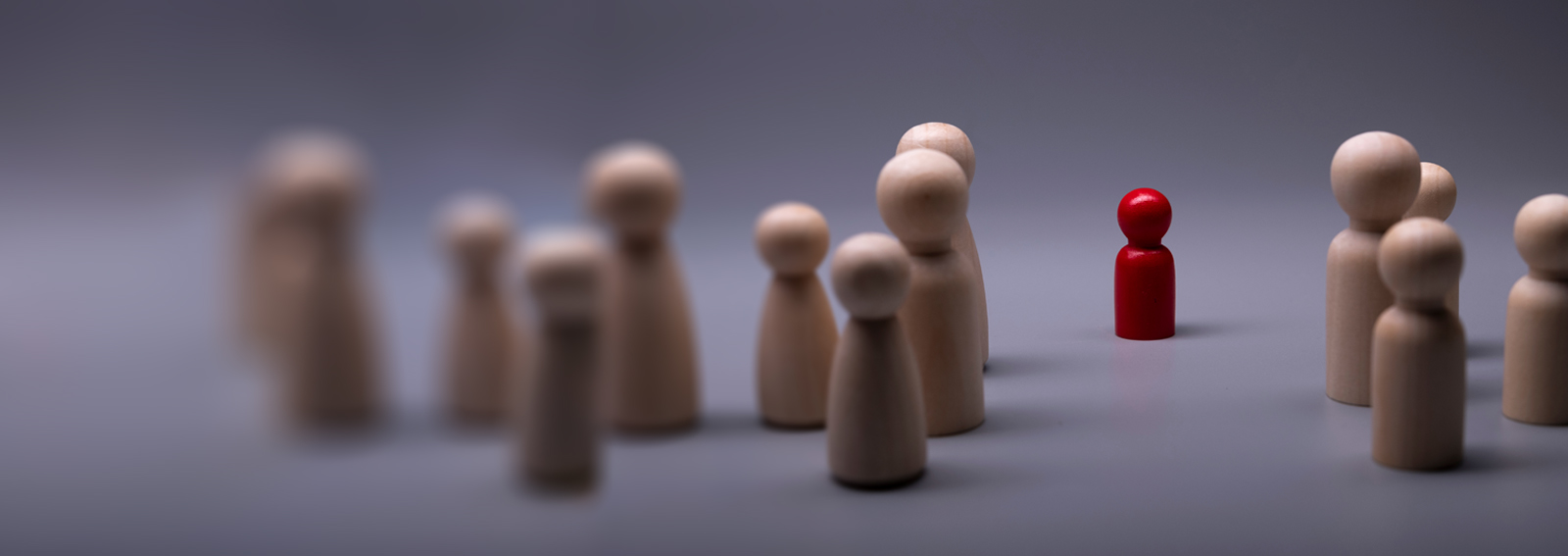 Group of wooden figurines and one red figurine standing in between 