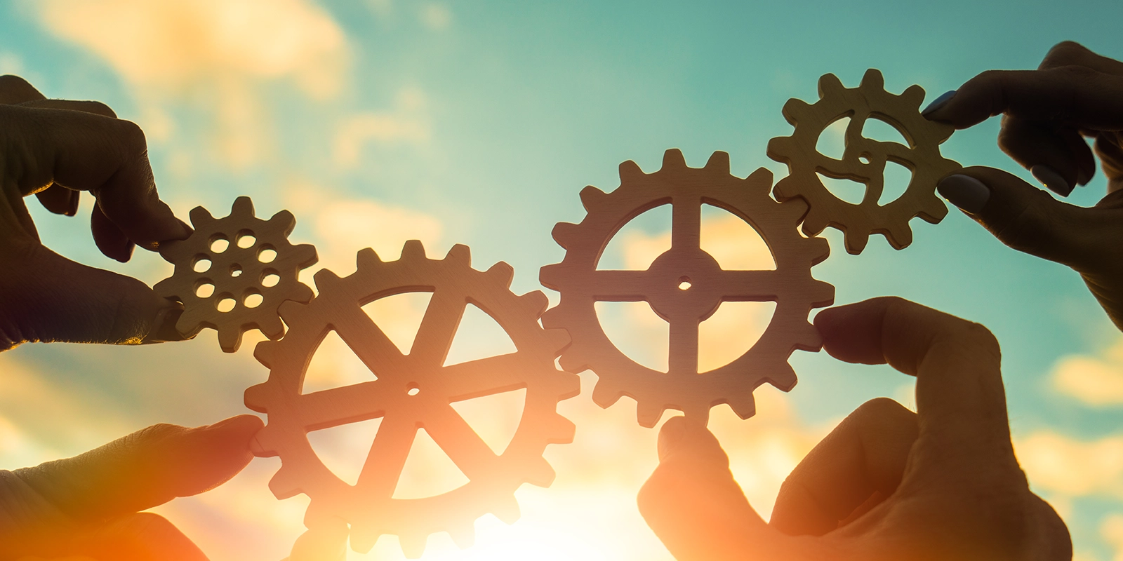 Four hands connecting gears together against the sky