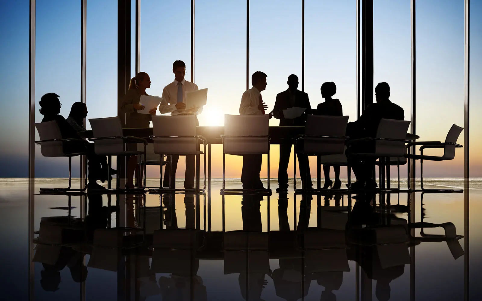 Eight people at a long table in front of floor to ceiling windows