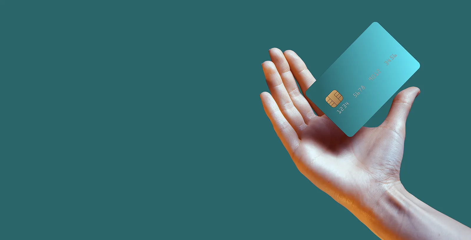 Womans hand holding a credit card on a teal background